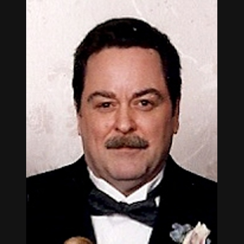 A close-up photo of John J. Dineen smiling in a suit and tie at a formal event