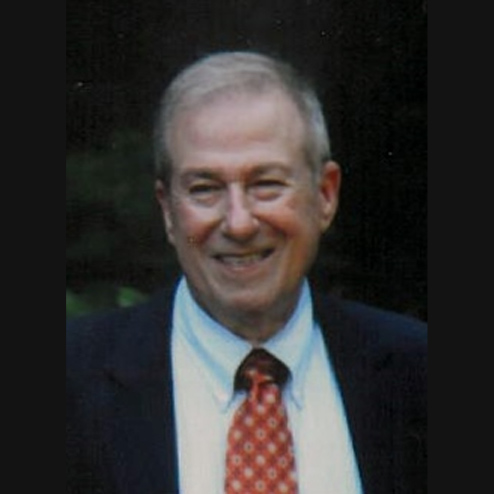 A candid photo of Rodney F. Sotka smiling at something in the distance while dressed in a suit and red tie