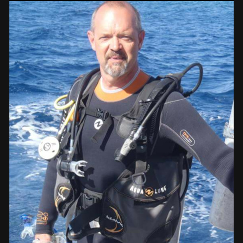 Douglas K. Crock posing for a photo while wearing his scuba diving suit out in the ocean