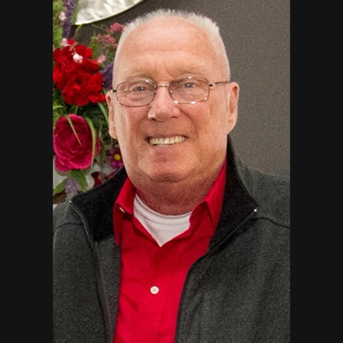 A close-up photo of James E. Corrigan smiling for the camera while wearing a red shirt and roses in the background
