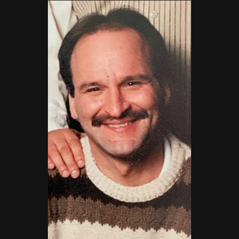 A close-up photo of Joseph "Marty" Kirincic smiling for the camera with a loved one's hand on him