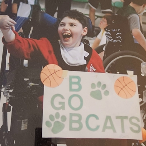 A close-up photo of Seth Joseph Kramer smiling and cheering at a sporting event proudly holding up a sign that says, "Go Bobcats"