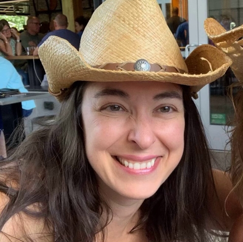 A close-up photo of Ana Grubiss smiling with friends wearing a cowgirl hat