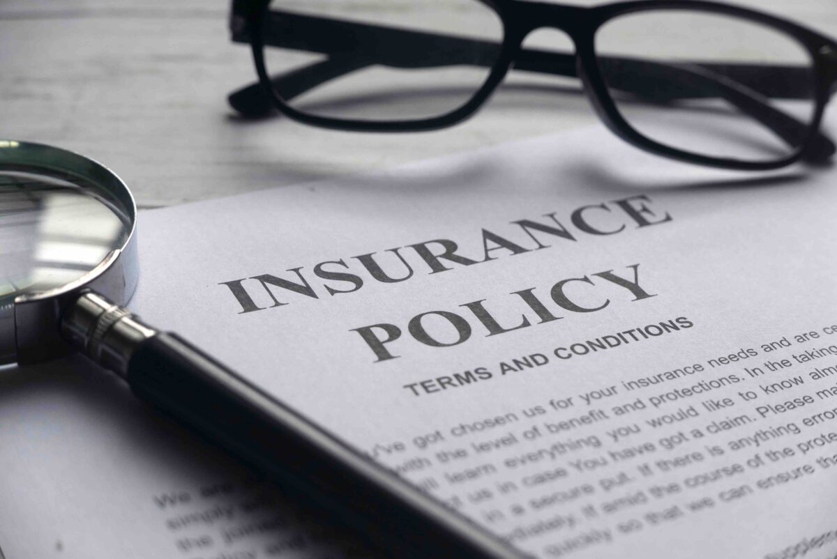 A piece of paper titled "Insurance Policy Terms and Conditions" laying flat on a table with glasses and a magnifying glass beside it